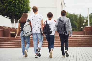 Dikiz aynası. Gündüz vakti üniversitenin yakınlarında günlük giysiler içinde bir grup genç öğrenci.