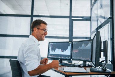 Heyecanlı ve mutlu. Zafer ve başarı kavramı. Resmi giyinmiş genç işadamı birden fazla ekranla ofiste..