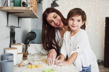 Kadınlar gülümserken yan tarafa bakmak. Mutlu kız ve anne birlikte fırın ürünleri hazırlıyorlar. Mutfakta küçük bir yardımcı..