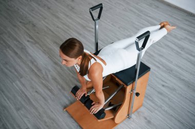 Hava görüntüsü. Sağlıklı merkezde zayıf vücutlu, kendine güvenen genç bir kadın özel ekipman kullanarak egzersiz yapıyor..