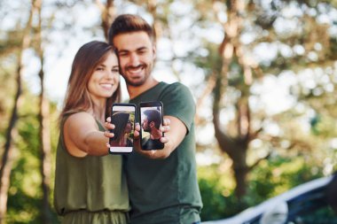 İki tane akıllı telefonu ellerinde tutuyorlar. Genç ve güzel bir çift gündüz vakti ormanda iyi vakit geçirir..