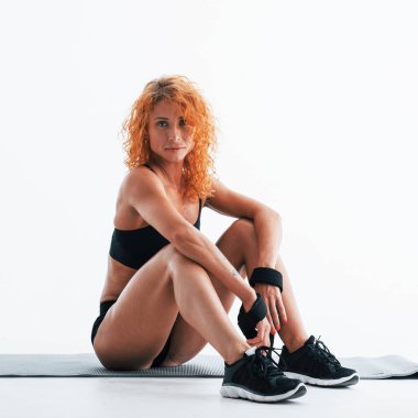 Paspasın üzerinde duruyor. Kızıl saçlı kadın vücut geliştirici beyaz arka planda stüdyoda..