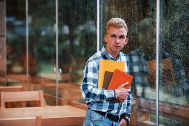 Not defterlerini elinde tutuyor. Yağmurlu bir günde kafede duran genç bir öğrencinin portresi. Bir kişi..