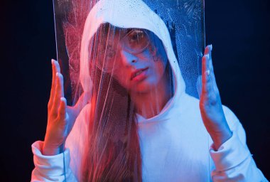 Islak ve berrak materyalleri tutuyor. Stüdyo karanlık stüdyoda neon ışıkla çekiliyor. Genç bir kızın portresi.