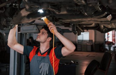 Kız arkada duruyor. Atölyedeki üniformalı adam modern arabanın kırık parçalarını tamir ediyor..