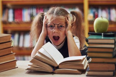 Heyecanlı hissettiriyor. Saçları örgülü şirin küçük kız kütüphanede. Kitaplardaki elma..