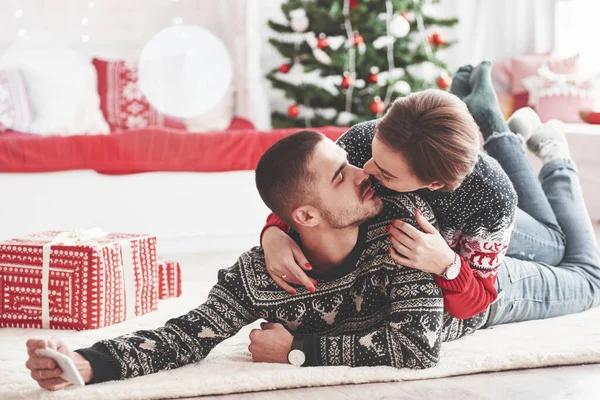 かわいいキスの写真を撮る 素敵な若いカップルがギフトボックスで新年のリビングルームの床に横たわっています — ストック写真