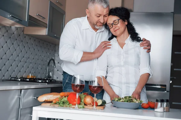 愛を感じる 台所で野菜を使った料理を作る白いシャツを着た男と妻 — ストック写真