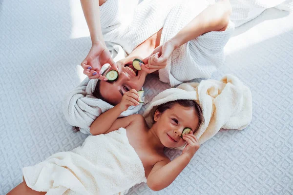 Young Positive Mother Daughter Towel Head Lying Bed Together Cucumber — Stock Photo, Image