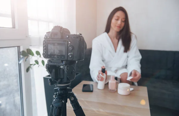 Black professional camera. In front of camera on the tripod. Conception of fashion and skincare. Brunette girl uses cosmetics.