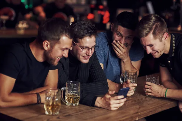 智能手机上有趣的内容 三个朋友手里拿着啤酒在酒吧休息 谈话时 — 图库照片
