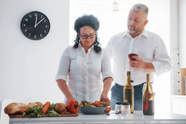 妻の後ろを歩く 台所で野菜を使った料理を作る白いシャツを着た男と妻 — ストック写真