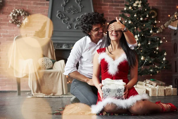 私が考える贈り物ですか 男はガールフレンドを驚かせている 新年のプレゼントを与える 若いカップルは休日の装飾された部屋の床に座っている — ストック写真