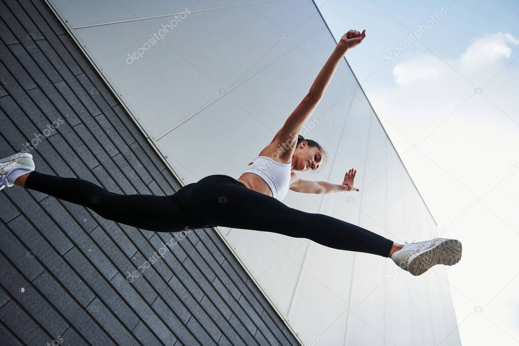 Bottom view. Young sportswoman doing parkour in the city at sunny daytime.