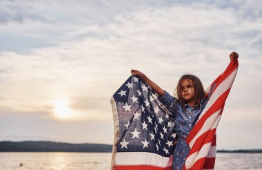 Amerikan Bayrağı elinde olan vatansever kadın çocuk. Bulutlu gökyüzüne karşı.