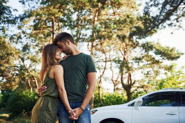 Beyaz otomobilin yanında duruyor. Genç ve güzel bir çift gündüz vakti ormanda iyi vakit geçirir..