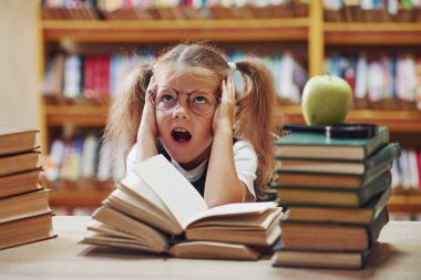 Heyecanlı hissettiriyor. Saçları örgülü şirin küçük kız kütüphanede. Kitaplardaki elma..