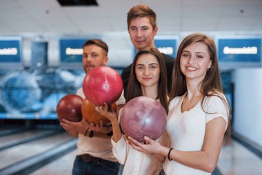 Topları elinde tutuyor. Genç neşeli arkadaşlar hafta sonları bowling kulübünde eğleniyorlar..