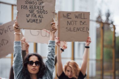 Kurbanlar dinlenmek ister. Bir grup feminist kadın dışarıda hakları için protesto yapıyor..