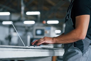 Modern laptop. Klavyede yazıyorum. Fabrikada sanayi işçisi. Turuncu şapkalı genç teknisyen..