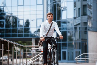 Arkadaki muhteşem modern iş binası. Siyah bisikletli resmi elbiseli adam şehirde..