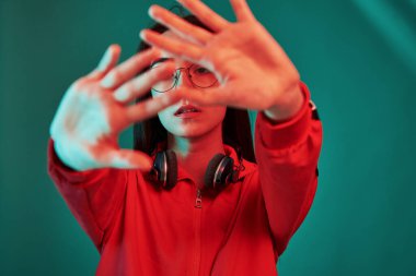 Kameranın önünde ellerini tutuyor. Stüdyo içeride neon ışıkla çekiliyor. Güzel bir genç kızın portresi.