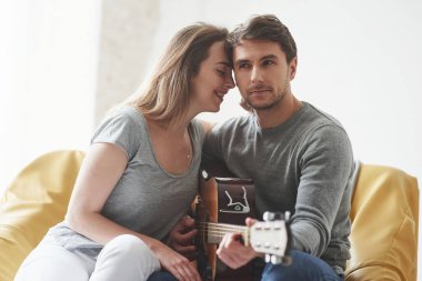 Sevimli genç insanlar. Yeni evin oturma odasında kız arkadaşına akustik gitar çalmak..