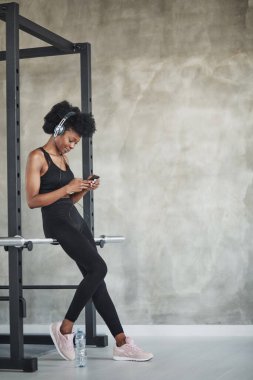 Tam boy fotoğraf. Kıvırcık saçlı ve spor elbiseli Afrikalı Amerikalı kadın spor salonunda spor yapıyor..