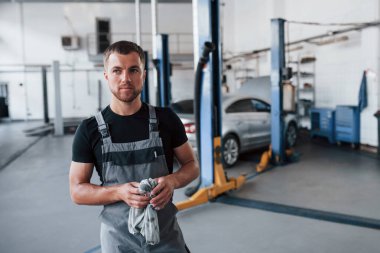 İyi iş çıkardın. Siyah gömlekli ve gri üniformalı adam bozuk arabayı tamir ettikten sonra garajda duruyor..