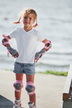 Arka planda göl kenarında paten kayan sevimli küçük bir kız..