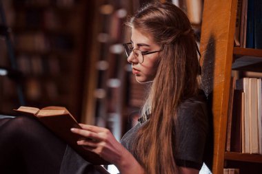 Yerde oturuyordu. Kütüphanede kitaplarla dolu bir kız öğrenci var. Eğitim kavramı.