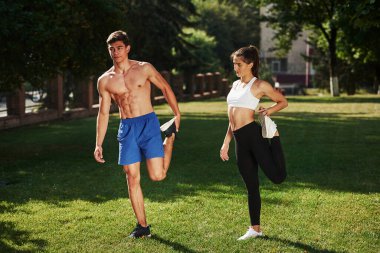 Erkeklerin güzel karın kasları var. Erkek ve kadının şehirde gündüz vakti parkta fitness günü var..