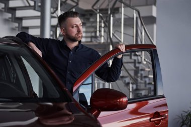 Zengin biri. Genç sakallı işadamının önü lüks kırmızı arabasının yanında duruyor..