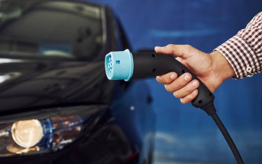 Adam elektrikli bir arabanın karşısında duruyor ve şarj halatını tutuyor..