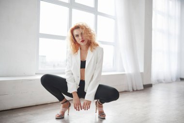 Oturma pozisyonu. Çekici kızıl saçlı kadın pencerenin yanındaki uzay odasında poz veriyor..