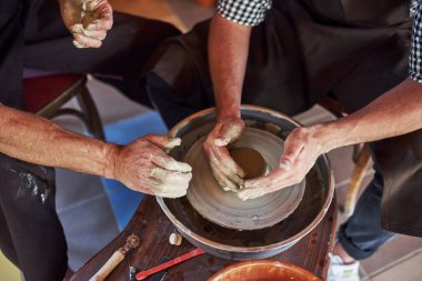 Manzarayı kapat. Usta öğrenci öğretiyor. İki seramik, el yapımı kil ürünü yapmak için çömlekçi çarkı kullanıyor..