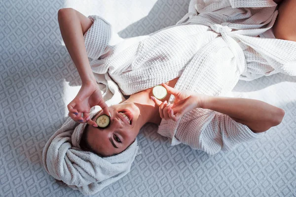 头戴毛巾的年轻阳性女人躺在床上撒着黄瓜 — 图库照片