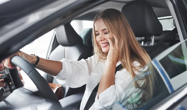 stock image Having conversation. Beautiful blonde girl sitting in the new car with modern black interior.