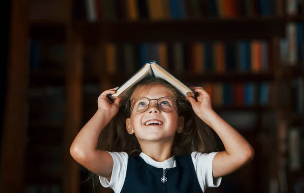Χαριτωμένο Κοριτσάκι Γυαλιά Στέκεται Στη Βιβλιοθήκη Γεμάτη Βιβλία Σύλληψη Της — Φωτογραφία Αρχείου