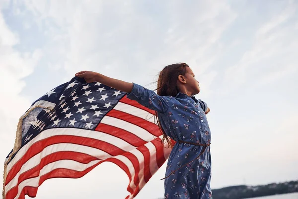 手里拿着美国国旗的爱国女孩在多云的天空下 — 图库照片