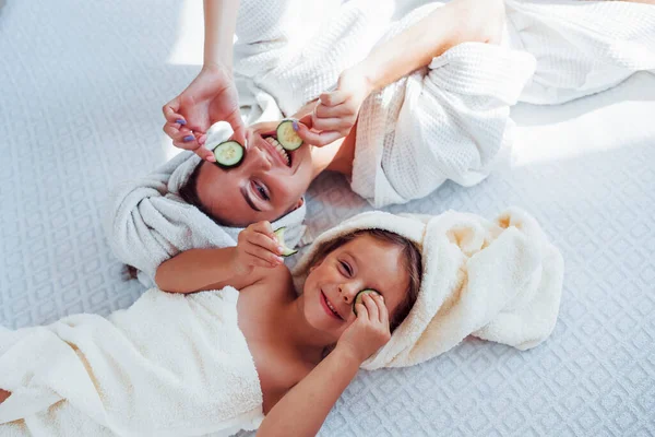 年轻的母亲和女儿头戴毛巾 头戴黄瓜 躺在床上 — 图库照片