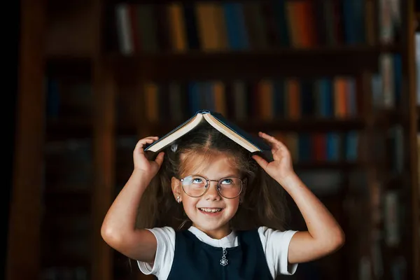 Χαριτωμένο Κοριτσάκι Γυαλιά Στέκεται Στη Βιβλιοθήκη Γεμάτη Βιβλία Σύλληψη Της — Φωτογραφία Αρχείου