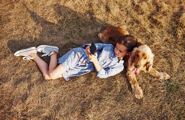 最上階だ 黒い電話で草の上に横たわる かわいい女の子持っていますA散歩とともに彼女の犬屋外で晴れた日 — ストック写真
