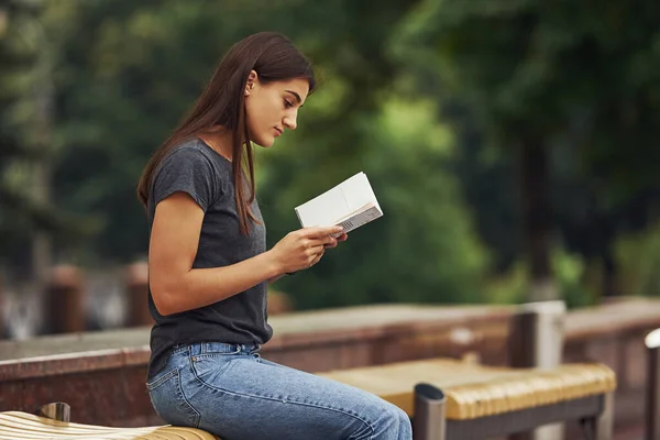 Young Brunette Sits Bench Reads Book Trees Background — Stock Photo, Image