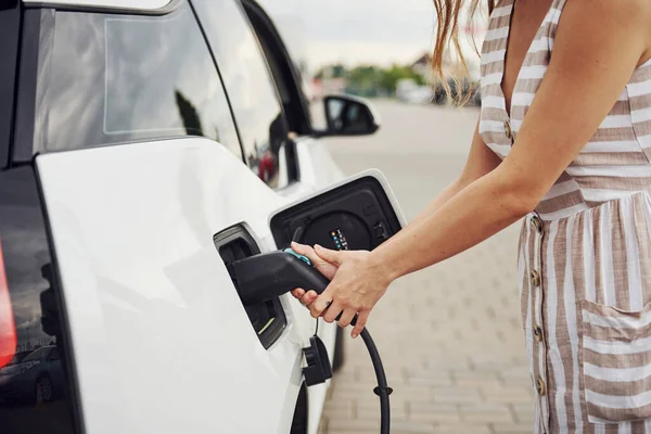Parçacık görünümü. Elektrikli arabalardaki kadın gündüz şarj istasyonunda. Yepyeni bir araç..