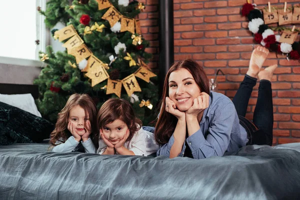 妈妈和两个孩子躺在床上 房间里装饰着圣诞树 — 图库照片