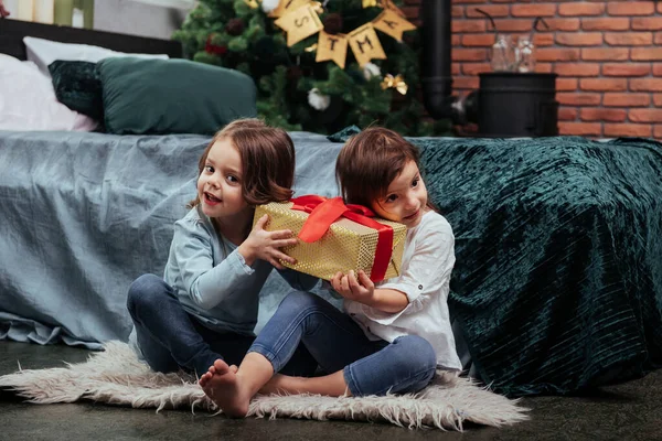 拿着那个黄色的盒子对里面的东西感兴趣送给这两个坐在床上漂亮房间里的孩子们的圣诞节礼物 — 图库照片