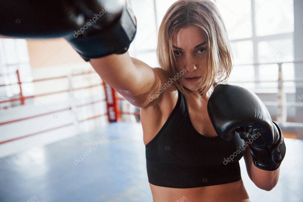 Captured from the front of she. Female sportswoman training in the boxing ring. In black colored clothes.