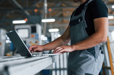 Modern laptop. Klavyede yazıyorum. Fabrikada sanayi işçisi. Turuncu şapkalı genç teknisyen..
