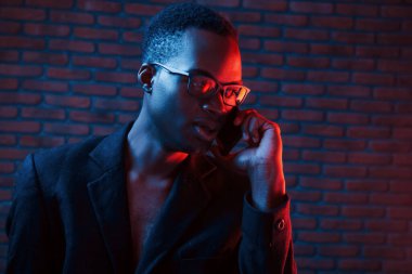 Telefon kullanarak sohbet ediyorlar. Fütürist neon ışıkları. Stüdyodaki Afrikalı Amerikalı genç adam..